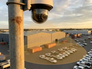 360-graden beveiligingscamera op metalen paal bewaakt industrieterrein met magazijnen en parkeerplaatsen tijdens gouden uur