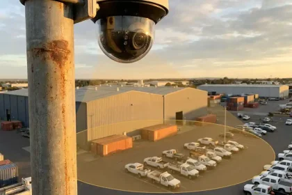 360-graden beveiligingscamera op metalen paal bewaakt industrieterrein met magazijnen en parkeerplaatsen tijdens gouden uur