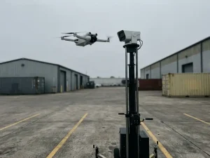 Witte surveillancedrone zweeft boven zwarte mobiele beveiligingscameratoren in industriële parkeerplaats met gele lijnen