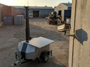 Mobiele bewakingscamera op telescoopstok naast vaste CCTV-camera op betonnen muur, beide gericht op industriële binnenplaats