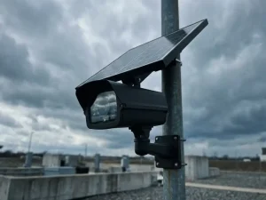 Zwarte zonnepaneel beveiligingscamera op metalen paal tegen bewolkte grijze hemel in industriële buitenomgeving